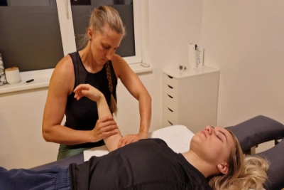 Liegende Person mit Ellenbogenverletzung - Physiotheapeutin behandelt Ellenbogen